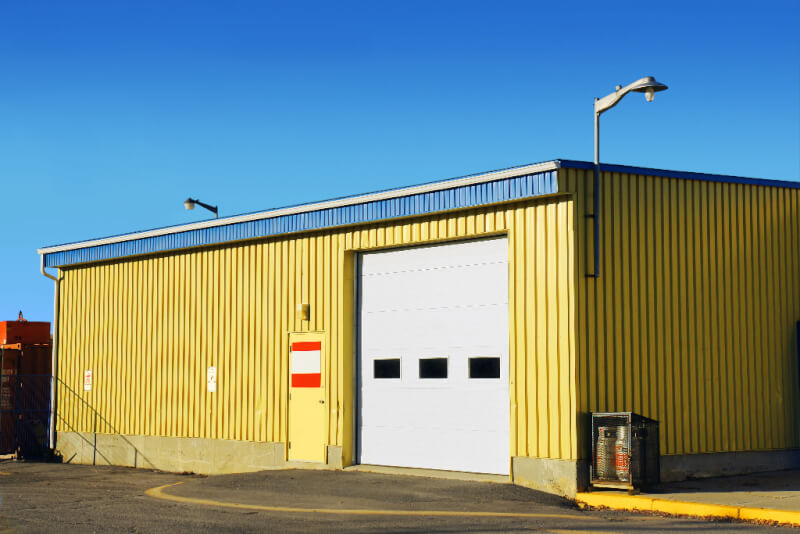 industrial Garage with yellow siding and one overhead door and one walk door